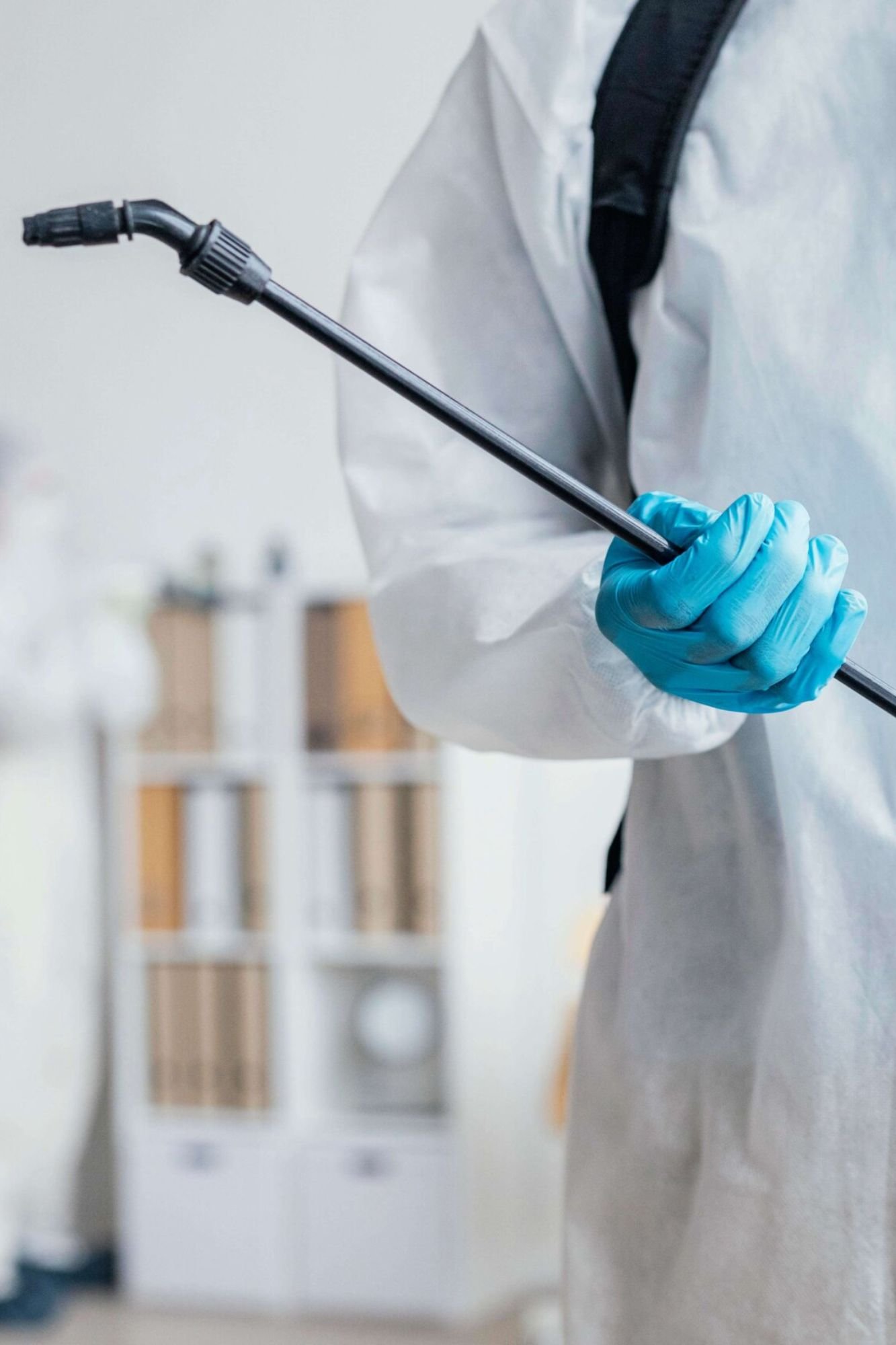 A person wearing a white coat and blue gloves holds a stick, representing a pest control service in Austin, TX.